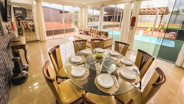 A dining area with a glass table set for six, surrounded by chairs. - Clube Relax & Lazer (Foz do Iguaçu)