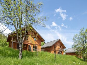 Eine Holzhütte mit Balkon, umgeben von üppiger Vegetation und blauem Himmel.