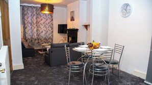 Ein Wohnzimmer mit einer Couch, einem Esstisch mit Stühlen, einem Kamin und einer Wanduhr.