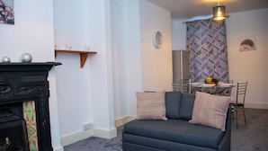 Ein Wohnzimmer mit einer Couch, einem Kamin, einem Esstisch mit Stühlen und einem gemusterten Vorhang.