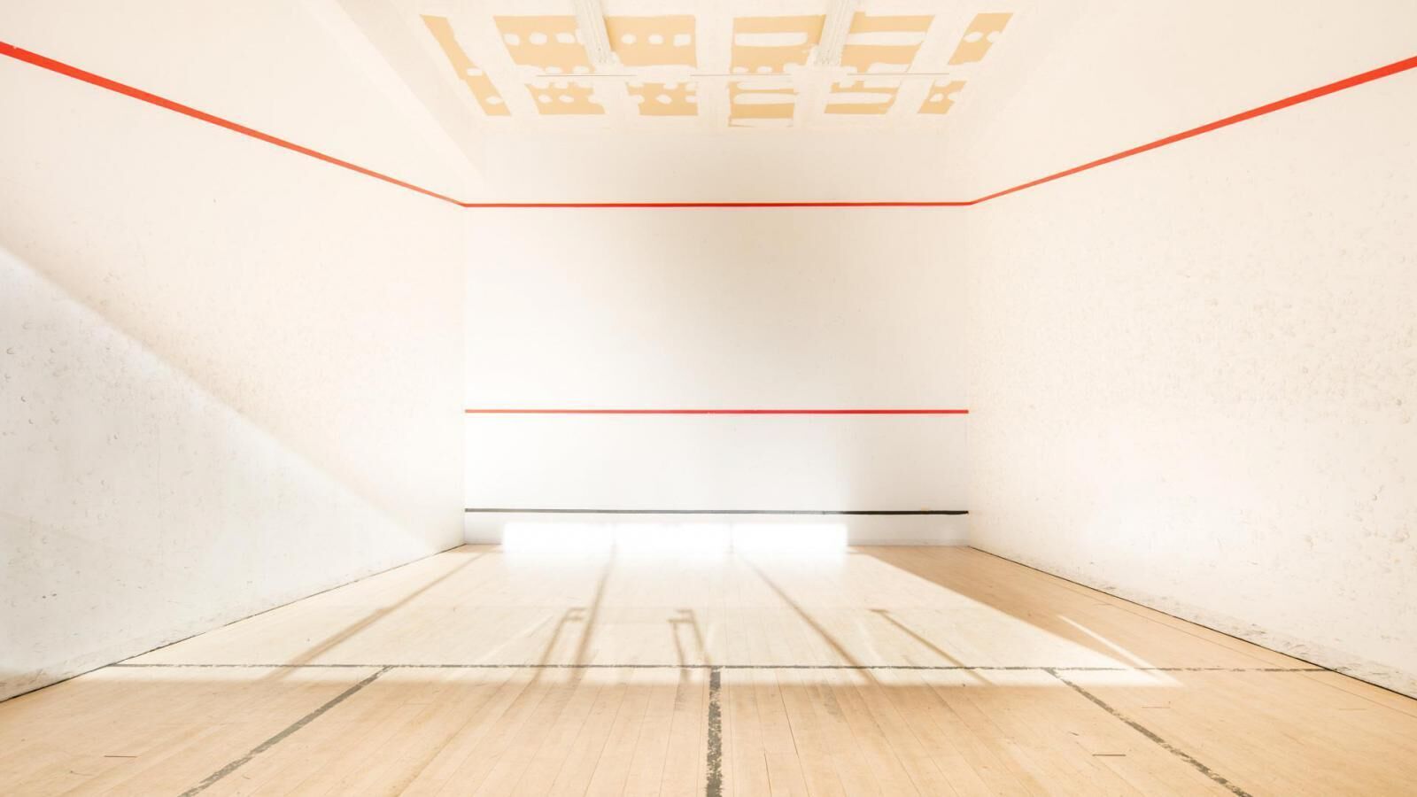 A room with a wooden floor, white walls, and a red and black line marking the floor.