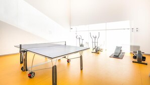 Una mesa de ping pong en una habitación luminosa, con equipo de ejercicio al fondo.