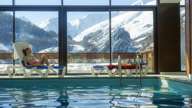Zona de piscina con sillones de descanso y vistas a montañas nevadas.