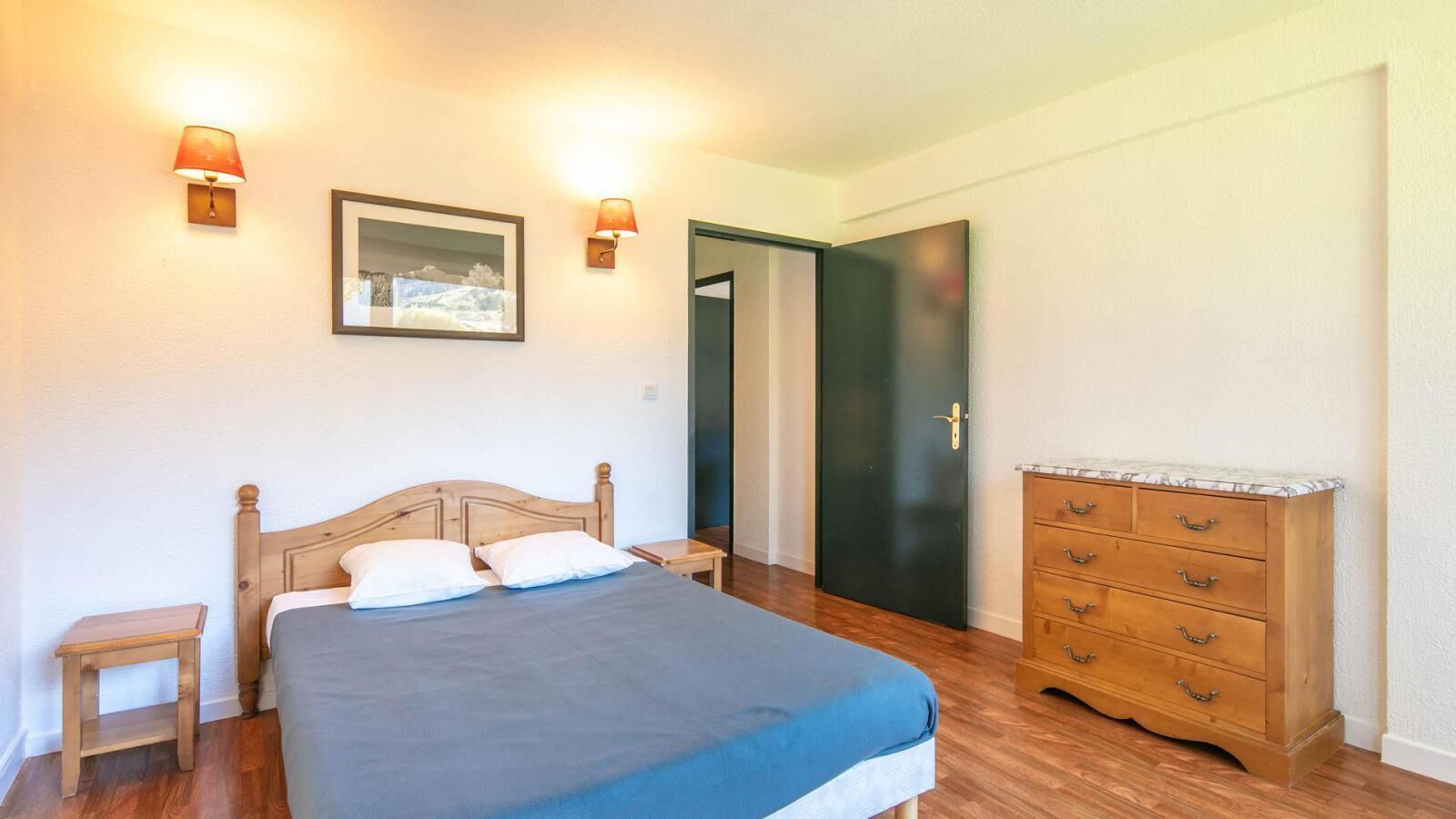 A bedroom with a bed, bedside tables, a dresser, and two wall-mounted lamps.