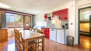 Cocina compacta con comedor, que incluye una mesa y sillas de madera, un refrigerador pequeño y gabinetes rojos.