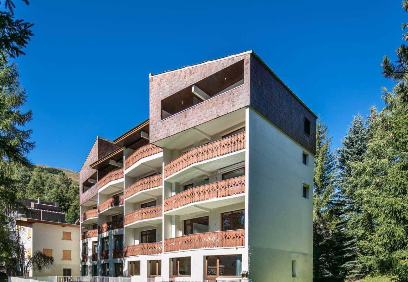A multi-story hotel with balconies, a stone facade, and a mountainous backdrop.