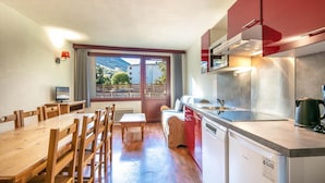 Habitación compacta con mesa de comedor, sillas, sofá, zona de cocina con fregadero y estufa, y un televisor.