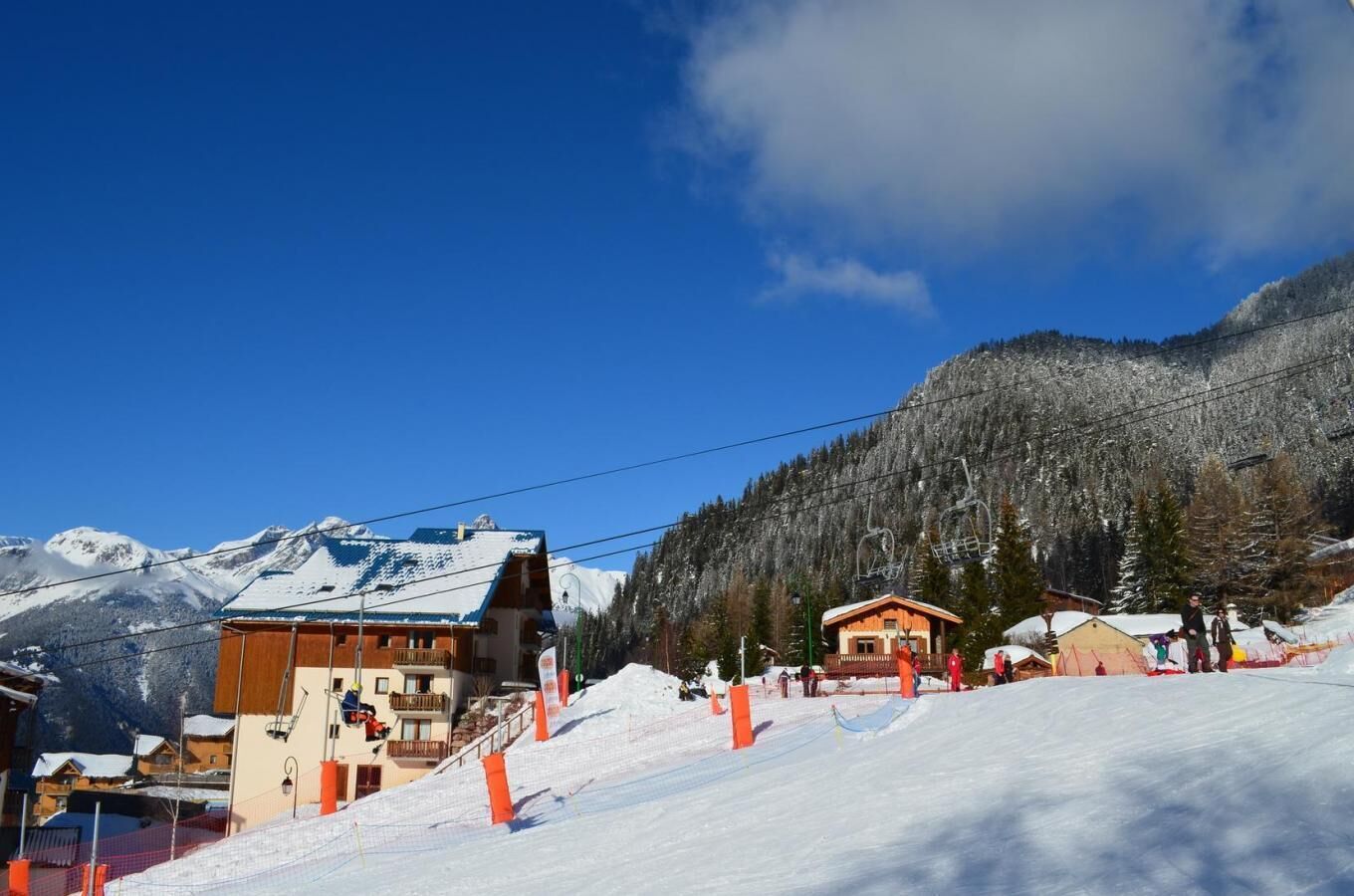 Een skioord met een houten lodge, skiliften en met sneeuw bedekte bergen.