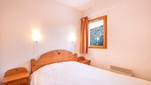 A bedroom with a wooden headboard, a single bed, two bedside tables, and a window with curtains. - 200m from resort center, swimming pool, sauna, tv, ski locker, 23m², Valfréjus (Valfréjus)