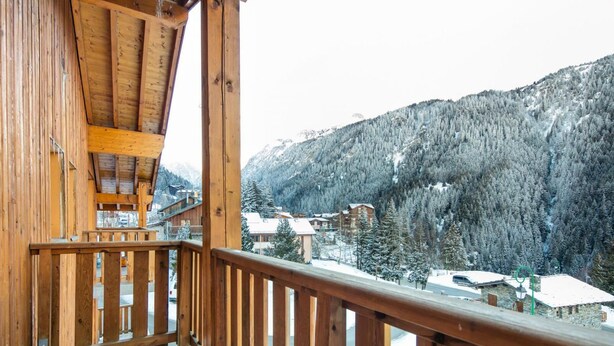 A wooden balcony with a view of snow-covered mountains and buildings. - 200m from resort center, swimming pool, sauna, tv, ski locker, 23m², Valfréjus (Valfréjus)