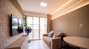 A modern living room with a sofa, a TV mounted on a brick wall, a dining table, and two standing fans. - Chaves do Atlântico (Cabedelo)