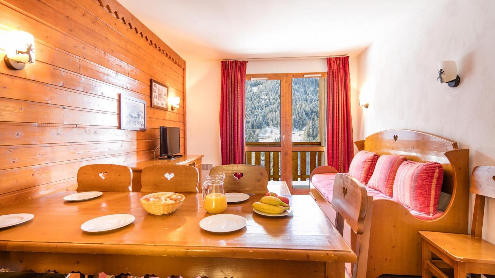 A wooden dining table with plates, a jug of orange juice, and a basket of bread.