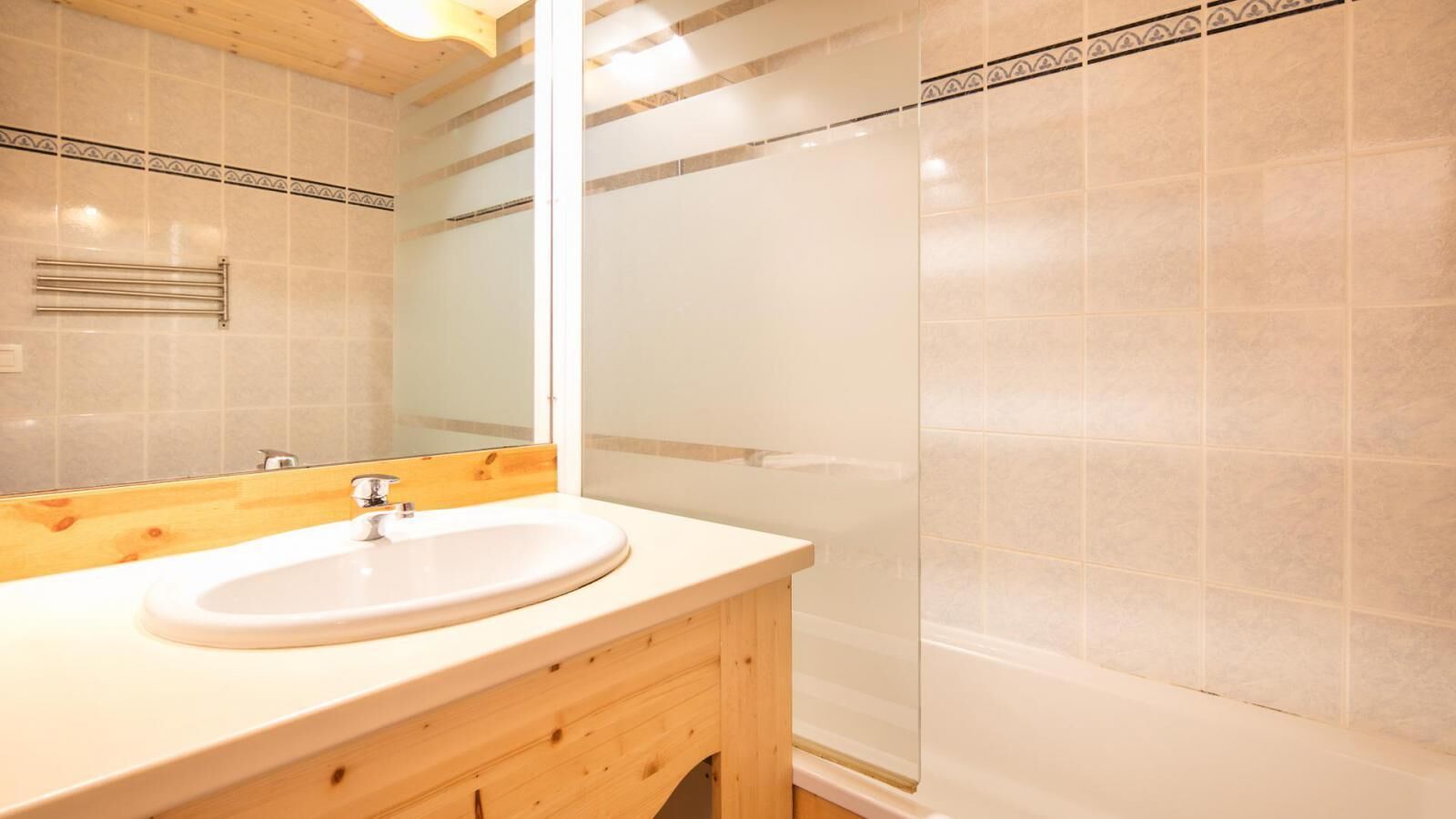 A bathroom with a wooden vanity, a white sink, and a glass shower enclosure.