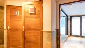 A hotel entrance with wooden double doors, a coat hanger sign, and a view of the outdoor area through glass doors.
