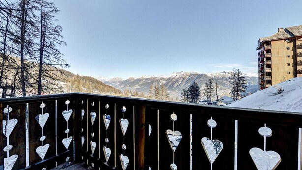 Een balkon met hartvormige decoraties en uitzicht op besneeuwde bergen.
