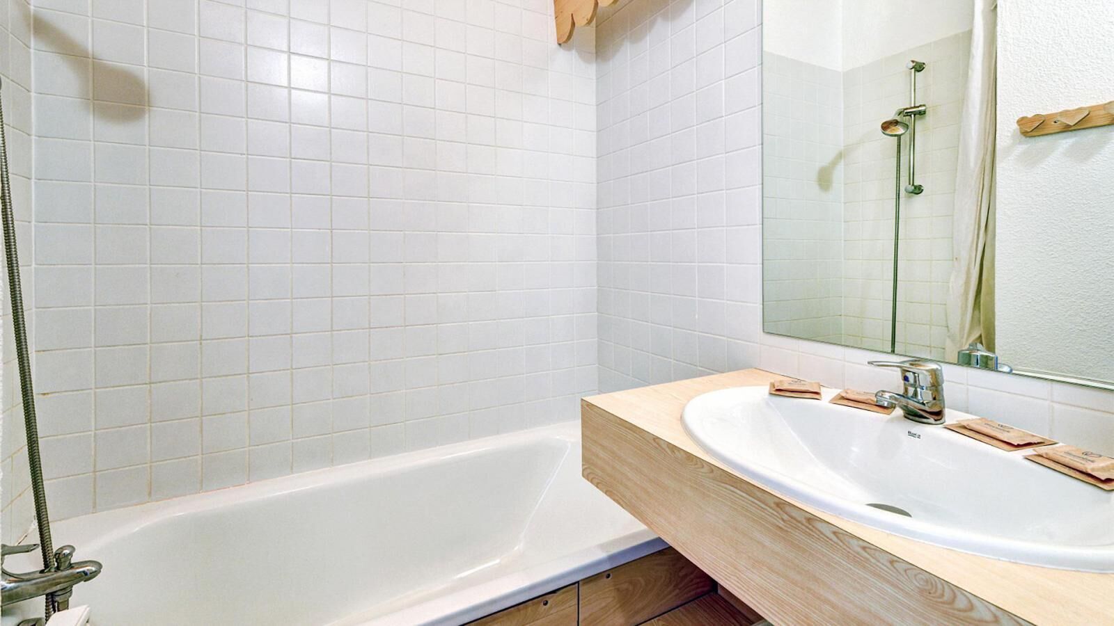 A bathroom with a white bathtub, a wooden vanity, and a mirror above the sink.