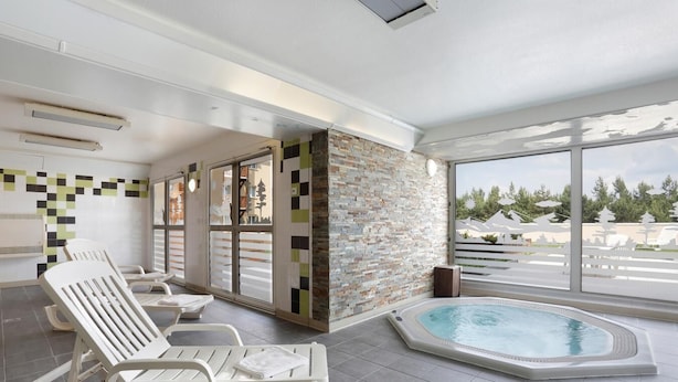 A modern indoor pool area with lounge chairs, a stone wall, and large windows offering a view of the outdoors. - Wifi, fitness, swimming pool, terrace, balcony, tv, ski locker, 41m², Pyrénées 2000 (Pyrénées 2000)