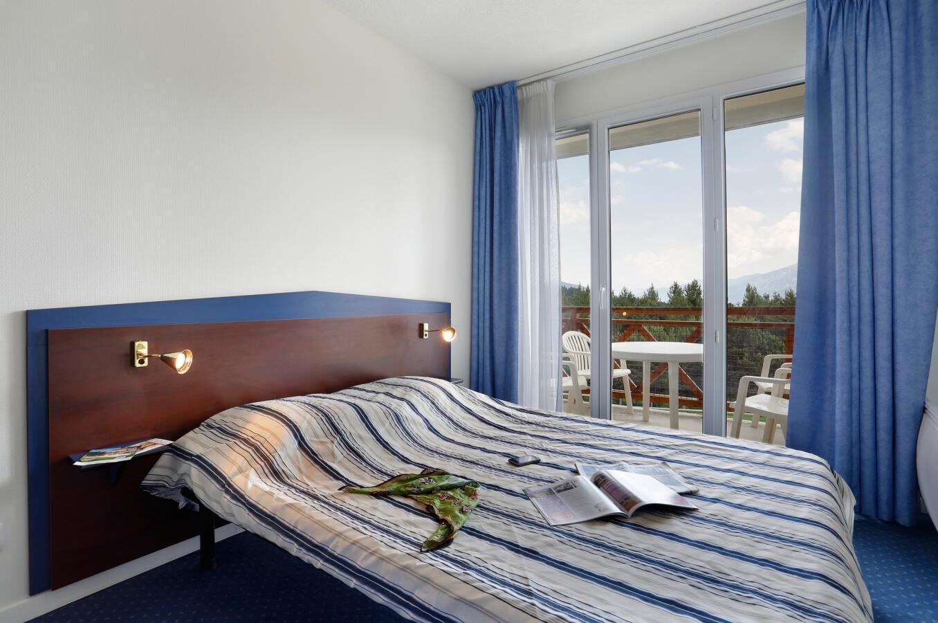 Een hotelkamer met een groot bed, een houten hoofdeinde, een raam met gordijnen en uitzicht op de omgeving.