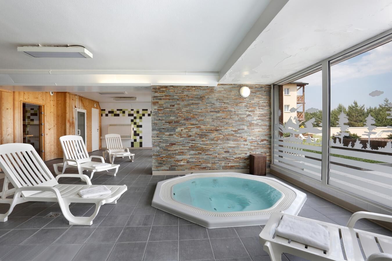 A modern indoor pool area with a stone wall, white lounge chairs, and a view of the outside.