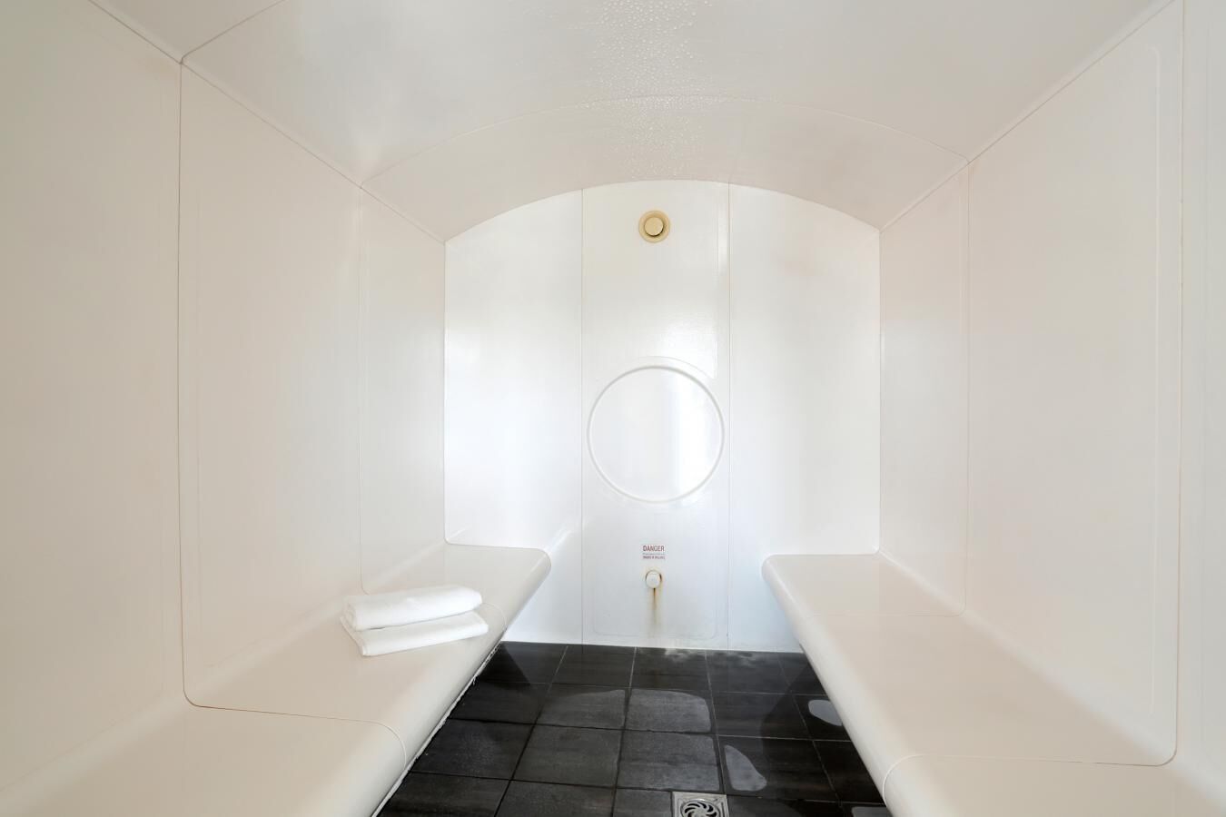 Ein modernes, minimalistisches Badezimmer mit einem großen Spiegel, zwei weißen Ablagen und einem schwarzen Fliesenboden.