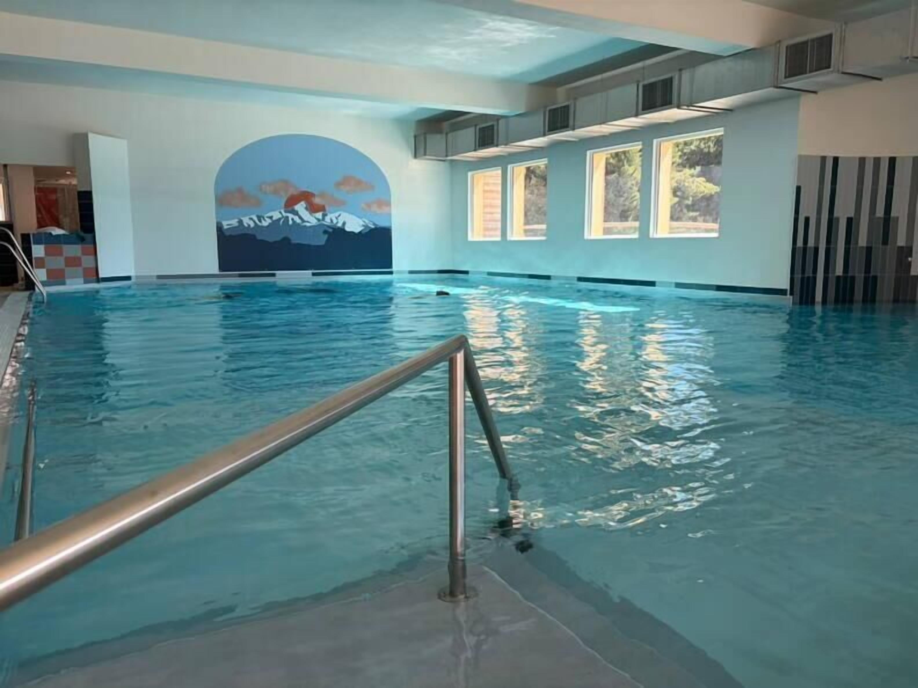 An indoor swimming pool with a view of mountains through a large window.