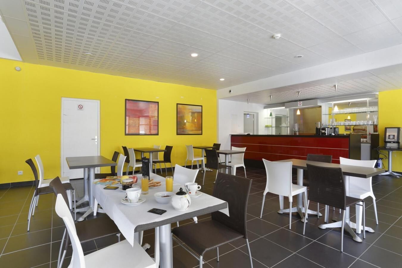 A dining area with tables and chairs, a counter, and a kitchen in the background.