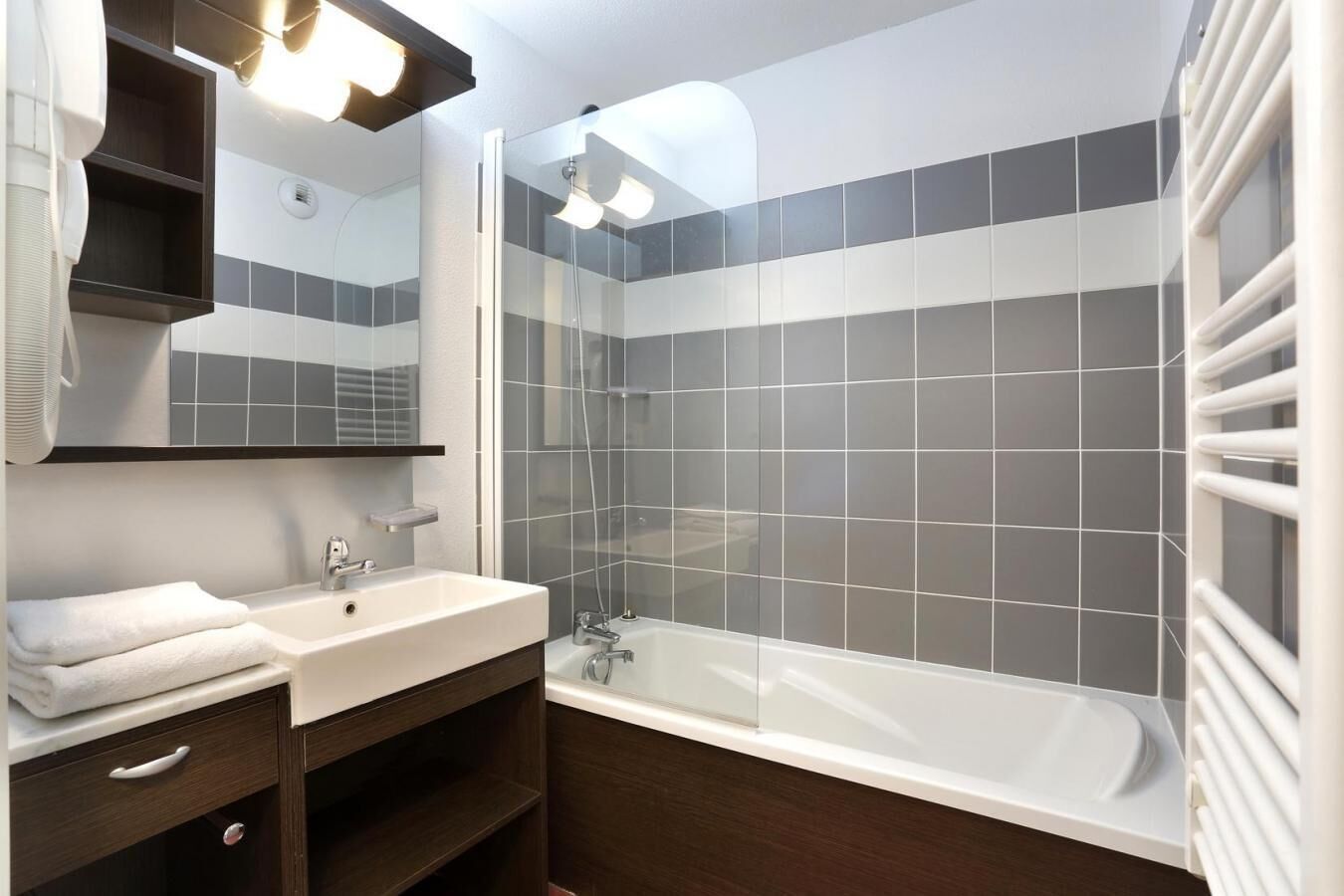 A modern bathroom with a white sink, a glass-enclosed shower, and grey and white tiles.