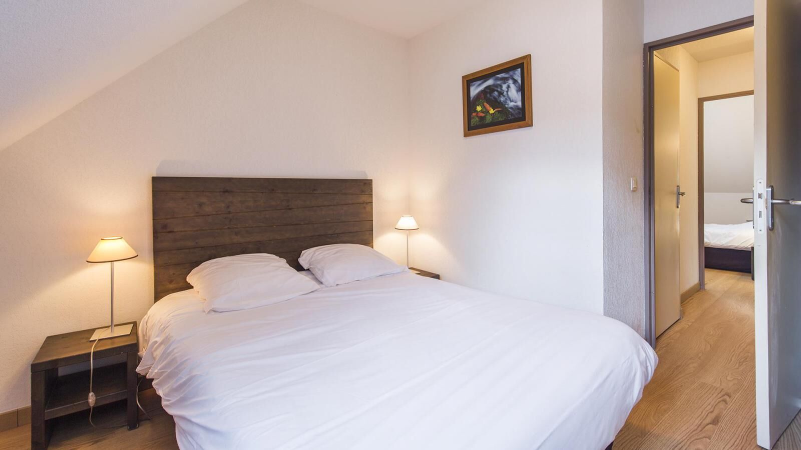 Un llit ben arropat amb llençols blancs en una habitació amb capçalera de fusta i dues làmpades laterals.
