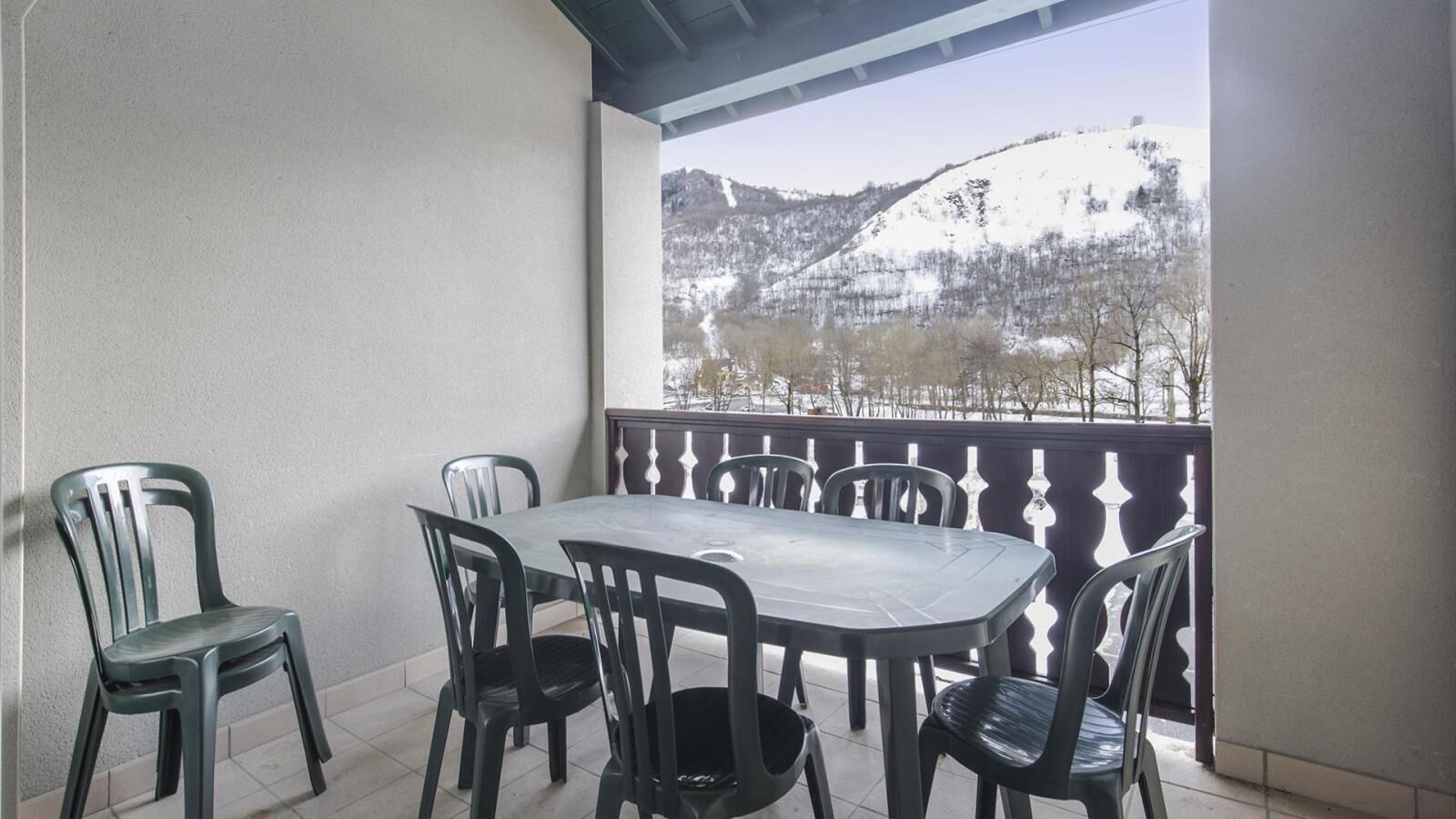 A balcony with a table and chairs, overlooking a snowy mountain landscape.