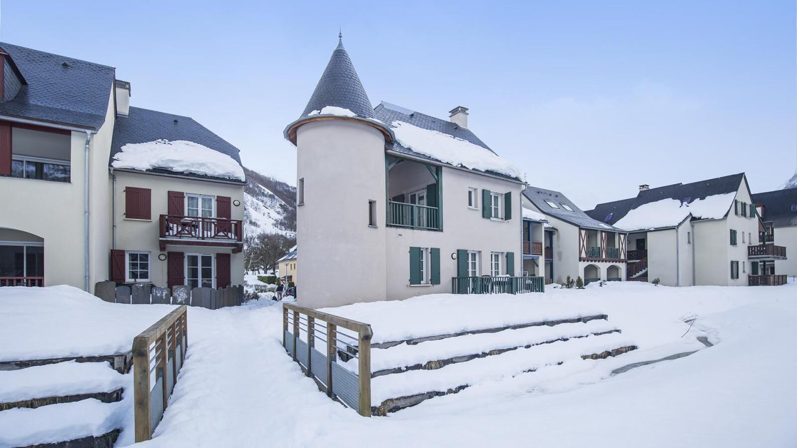 Une rue enneigée bordée de bâtiments à l’architecture européenne traditionnelle, dont l’un est doté d’une tourelle et d’un balcon.