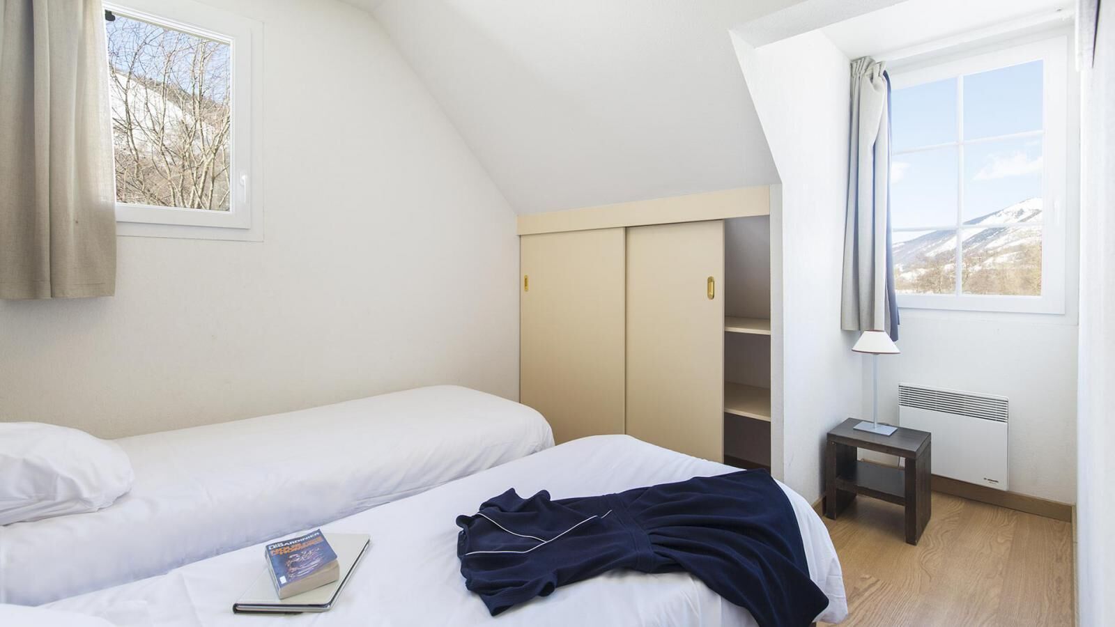 Un dormitorio con dos camas, un armario, un radiador y una ventana con vistas a las montañas.
