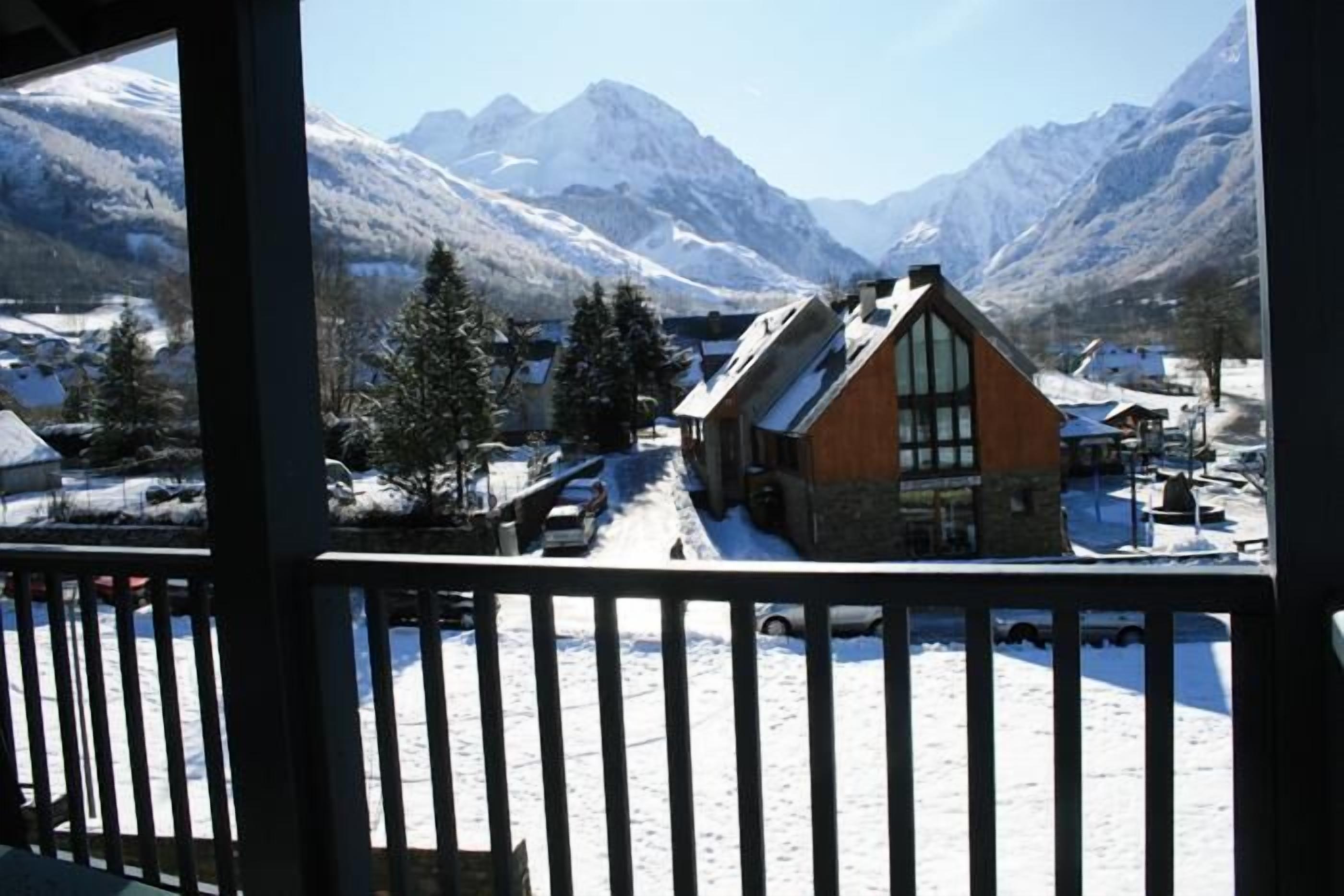 Un chalet de montagne avec une façade en bois et de grandes fenêtres, entouré de montagnes enneigées et surplombant un ciel dégagé.