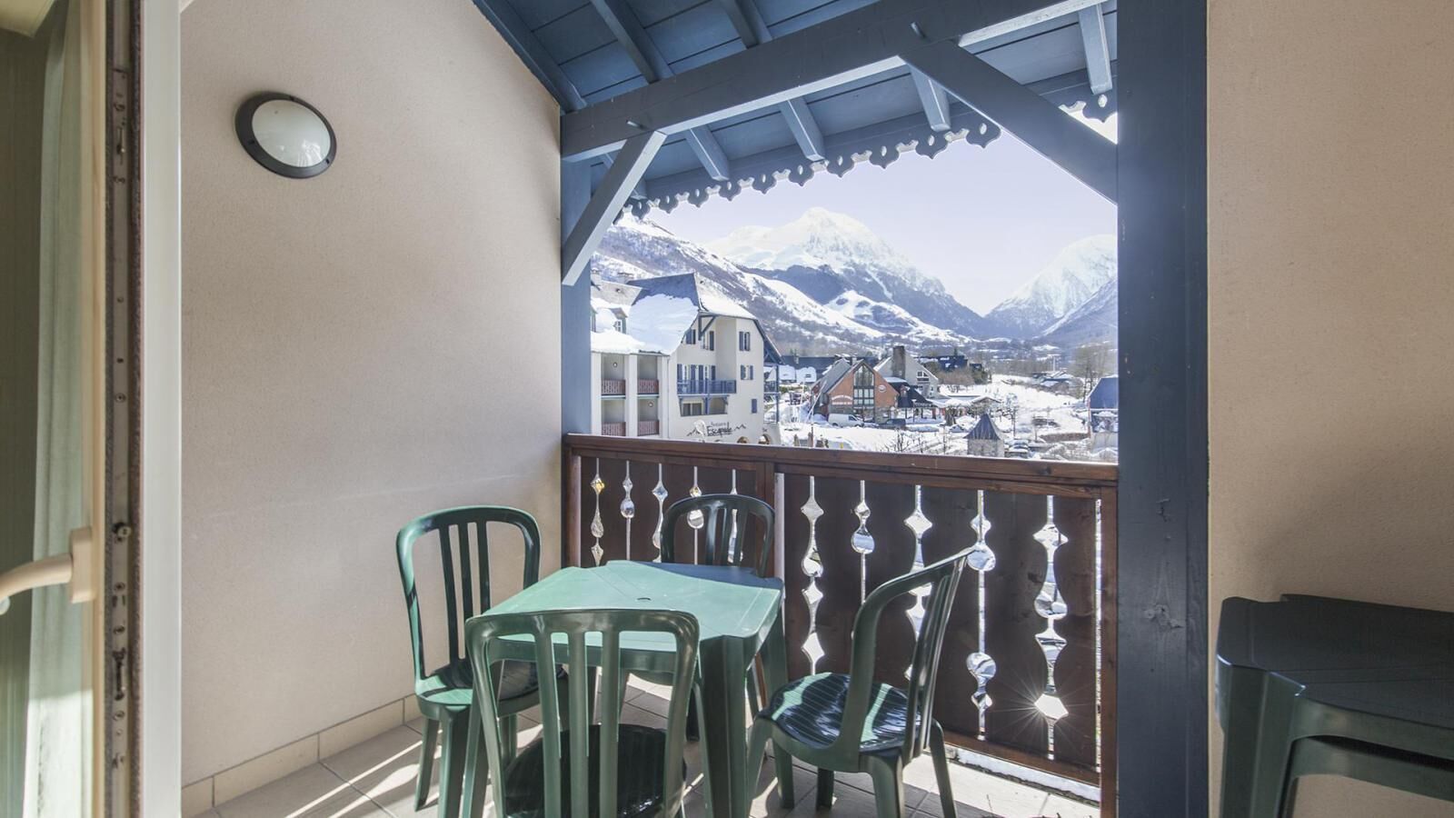 A balcony with a table and chairs, a view of snow-covered mountains, and a wooden railing.
