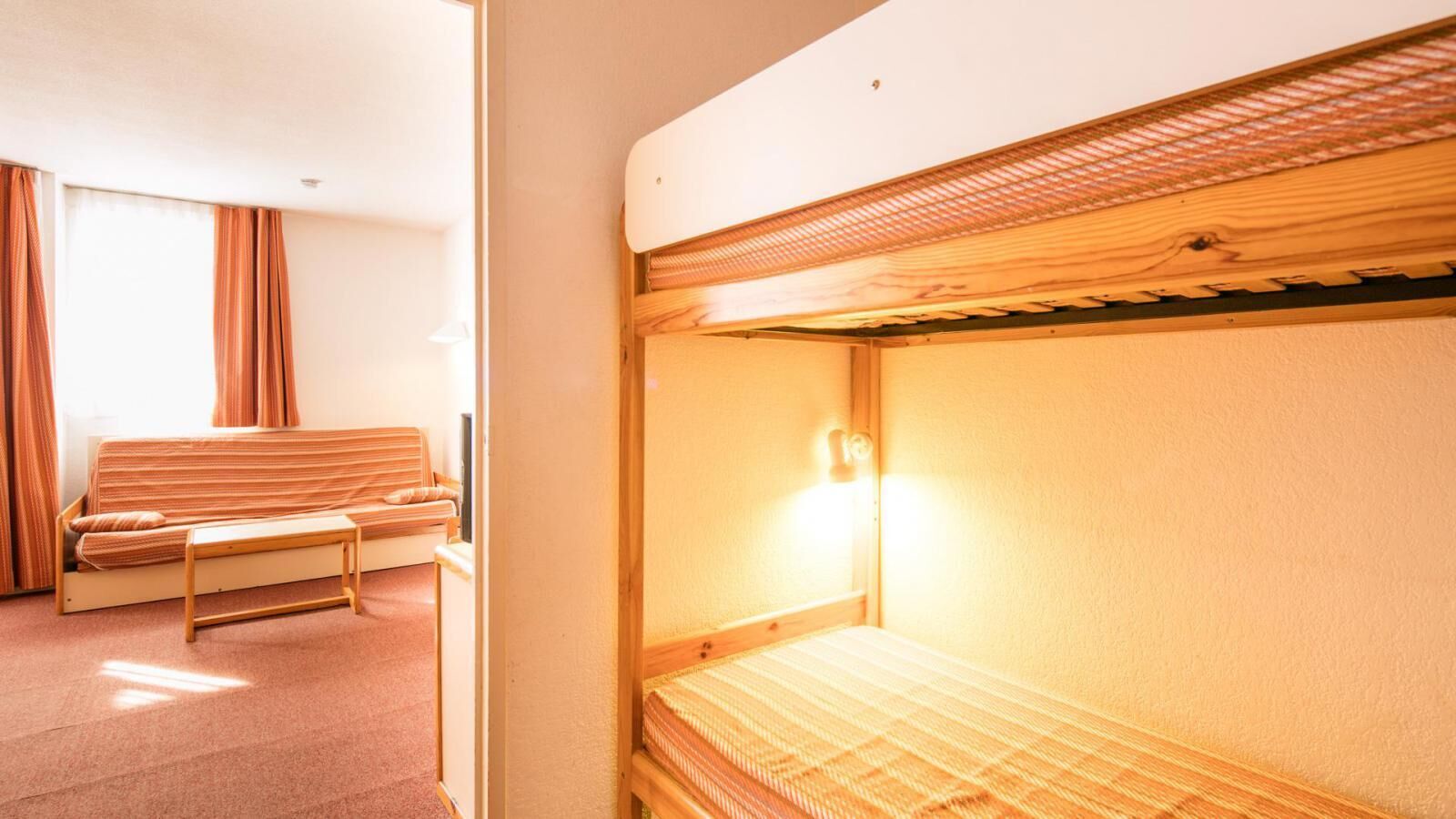 A bunk bed with a headboard, a bedside table, and a wall-mounted light.