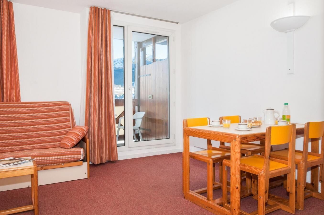 A room with a sofa, a dining table with chairs, a window with curtains, and a view of a snowy landscape.