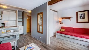 Un espacio habitable compacto con kitchenette, un sofá rojo, un espejo con marco de madera y un cuadro en la pared.