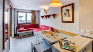 Una habitación acogedora con un sofá rojo, una mesa de comedor de madera y una lámpara colgante.