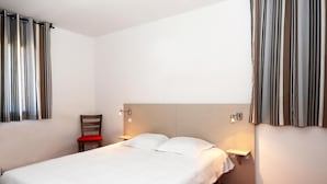 Hotellihuone, jossa on yksi sänky, yöpöytä, tuoli ja kaksi seinään kiinnitettyä lamppua.