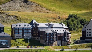 A modern hotel with multiple buildings, a parking area, and a hilly landscape in the background.
