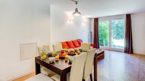 A dining area with a table set for breakfast, a sofa with orange cushions, and a large window with curtains. - 300m from ski slopes, swimming pool, parking, tv, ski locker, 40m², La Féclaz (Les Déserts)