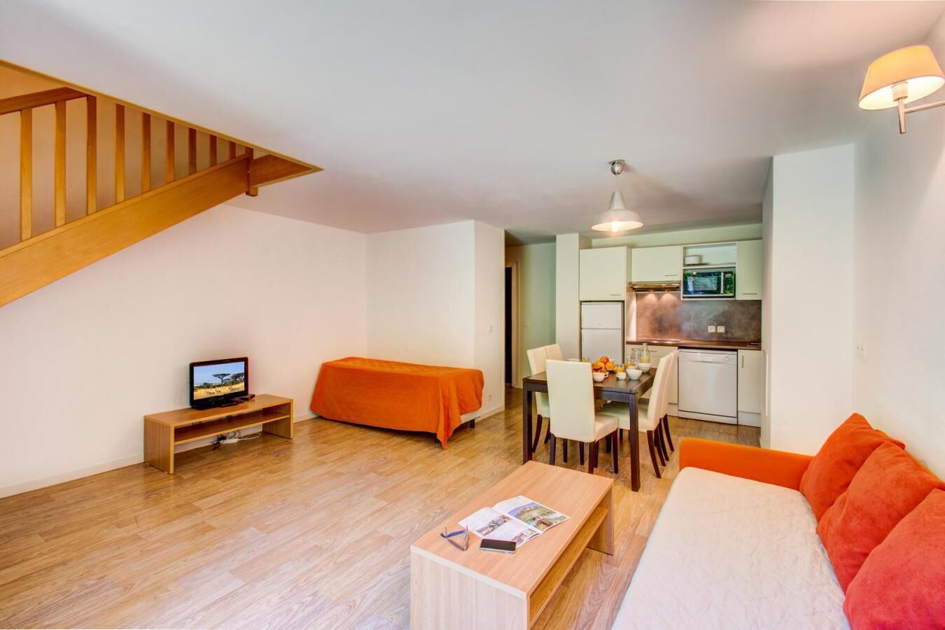 A compact living space with a dining area, kitchenette, and a TV on a wooden stand.