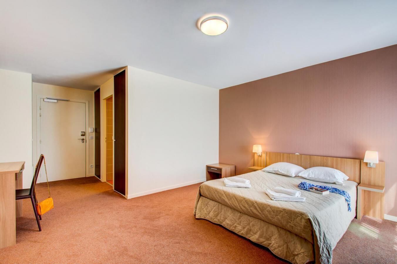 A hotel room with a bed, bedside tables, a desk, and a chair.