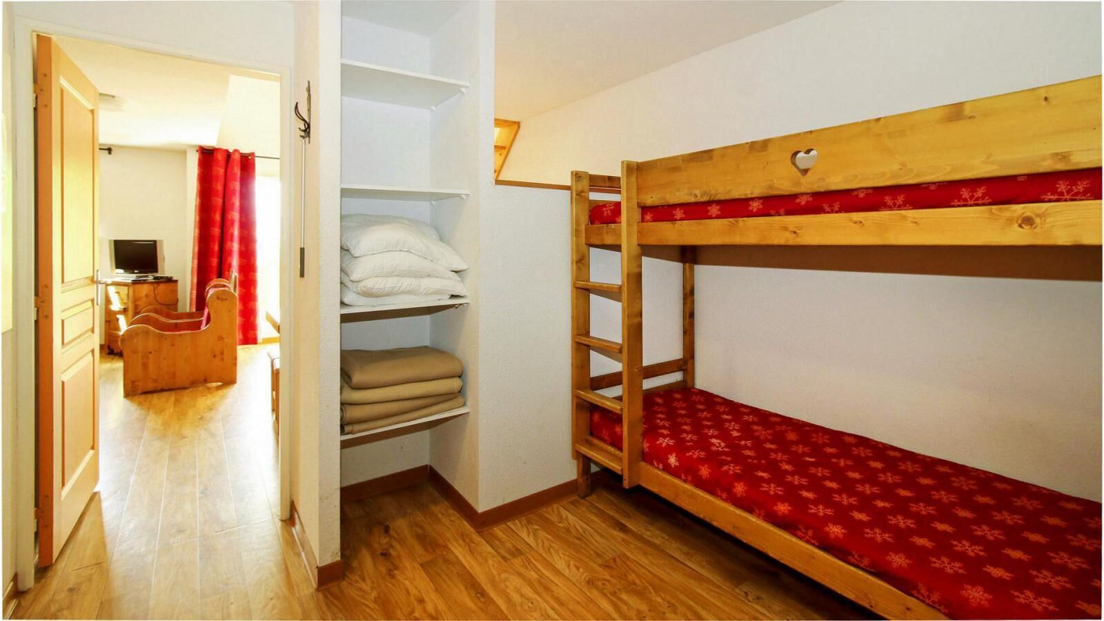 A room with a bunk bed, a wooden desk, and a shelving unit with folded blankets.