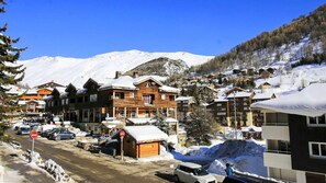 Un pueblo de montaña cubierto de nieve con edificios de madera, un cielo azul despejado y una calle con coches aparcados.