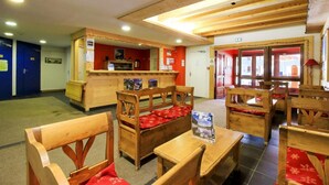 A restaurant with wooden furniture and red cushions. There are tables and chairs arranged for dining.