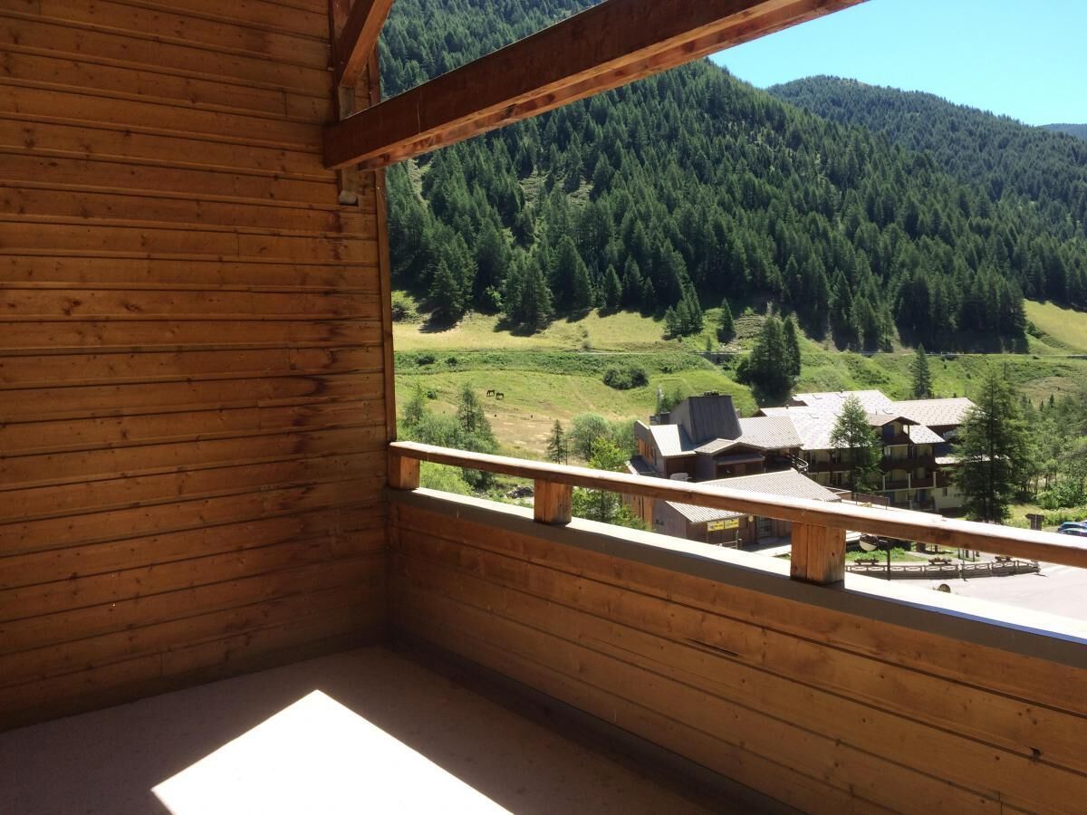 Una cabaña de madera con un balcón que da a un valle boscoso y edificios pequeños.