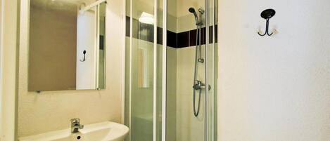 A bathroom with a glass shower enclosure, a sink, and a mirror.