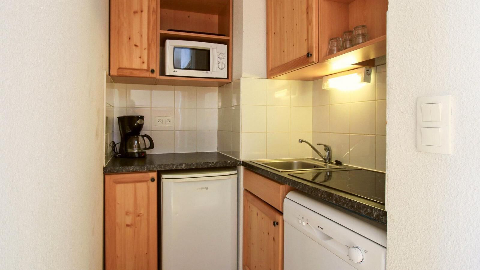 A compact kitchen with wooden cabinets, a microwave, a coffee maker, and a dishwasher.