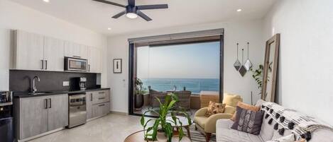 Eine moderne Wohnung mit Küche, Essbereich und Wohnzimmer. Sie verfügt über eine große Schiebeglastür, die auf einen Balkon mit Meerblick führt.