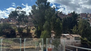 A rooftop terrace with a tiled floor, a railing, and a view of a residential area with trees and buildings.